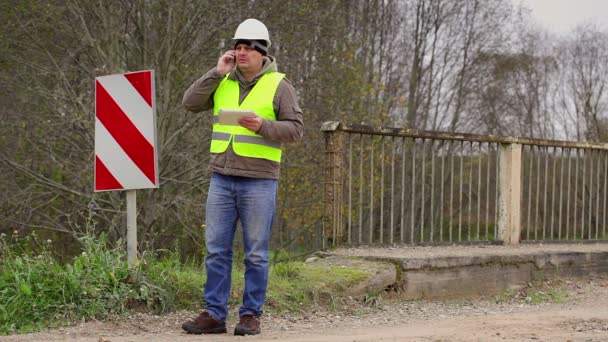 Ingenieur met mobiele telefoon in de buurt van brug defensie belemmeringen — Stockvideo