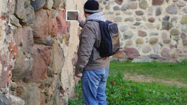Турист с планшетным ПК возле древней стены — стоковое видео
