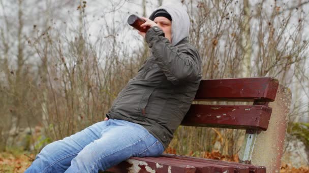 Homem com garrafa de cerveja no banco no outono — Vídeo de Stock