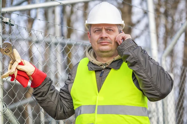 Worker with cell phone and adjustable wrench at outdoors — Stock Photo, Image