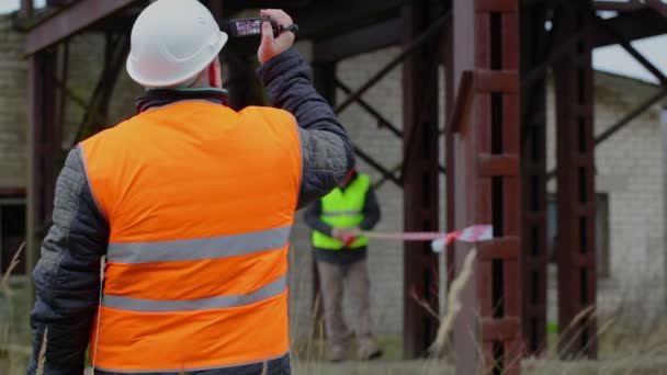 Inspector de edificio con videocámara y con trabajador en segundo plano — Vídeos de Stock