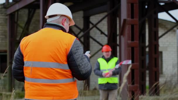 Building inspector with cell phone and with worker in background — Stock Video