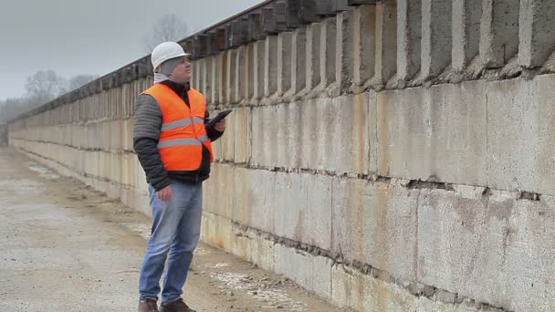 Engineer with tablet PC walking near the concrete wall — Stock Video