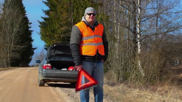 Человек с предупреждающим треугольником на дороге возле машины — стоковое видео