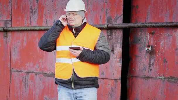 Arbetaren talar i mobiltelefon nära dörren av metall — Stockvideo