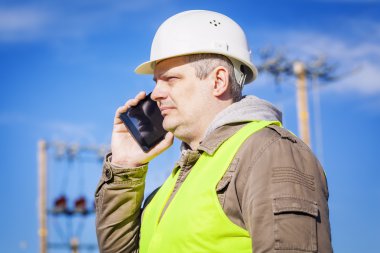 Elektrik mühendisi açık havada cep telefonuyla konuşuyor