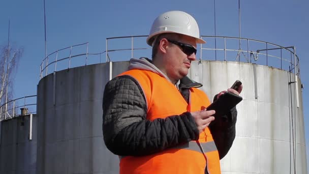 Ingeniero con teléfono celular y tablet PC cerca del tanque de aceite — Vídeos de Stock