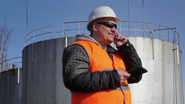 Glücklicher Arbeiter telefoniert in der Nähe von Öltank — Stockvideo