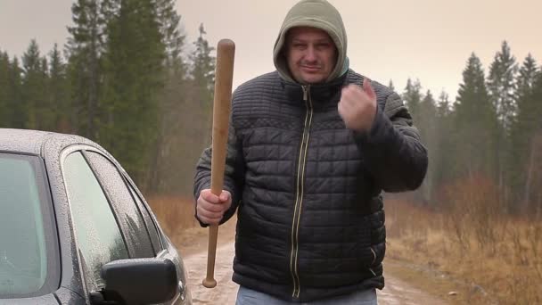 Hombre agresivo con un bate de béisbol cerca de coche en días lluviosos — Vídeo de stock