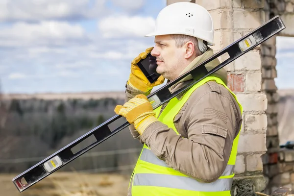 Építőmunkás, szintje és a mobiltelefon — Stock Fotó