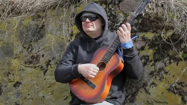 Человек, играющий на гитаре у старой стены — стоковое видео