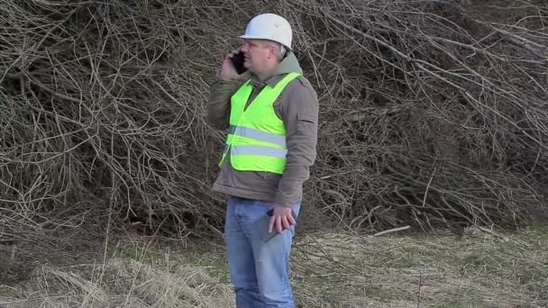 Forest ingenieur praten op mobiele telefoon in de buurt van stapel van twijgen — Stockvideo