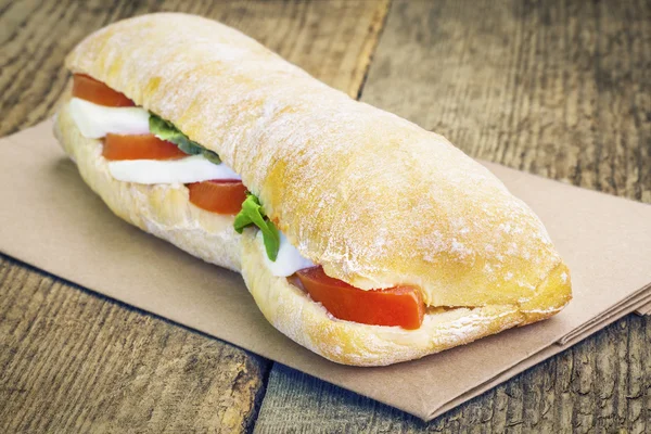 Filled baguette with mozzarella cheese on the old table — Stockfoto