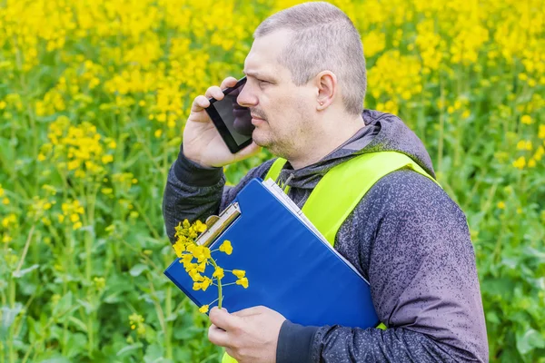 Agricultor con carpeta y teléfono celular cerca del campo de violación amarillo —  Fotos de Stock