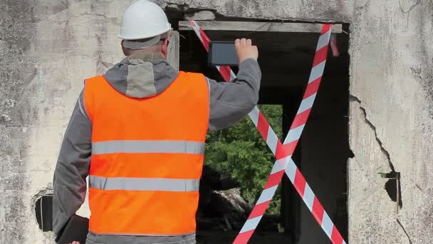 Employé de la construction filmé avec tablette PC près du bâtiment endommagé — Video