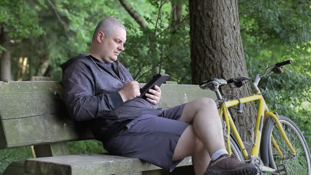 Man met tablet Pc in de buurt van fiets in het park — Stockvideo