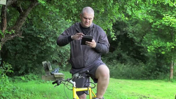 Άνθρωπος με Pc ταμπλετών με ποδήλατο στο πάρκο — Αρχείο Βίντεο