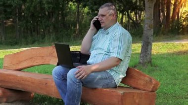 Parkta telefon ve dizüstü bilgisayar kullanan adam