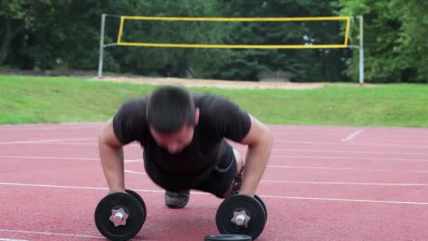 Teenager do push ups at outdoor on dumbbells — Stock Video