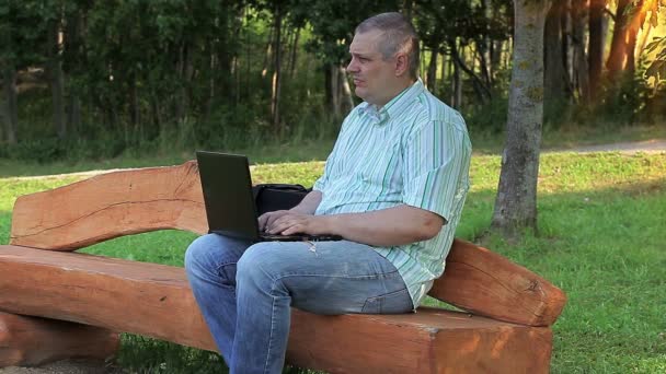 Uomo che utilizza il computer portatile nel parco sulla panchina — Video Stock