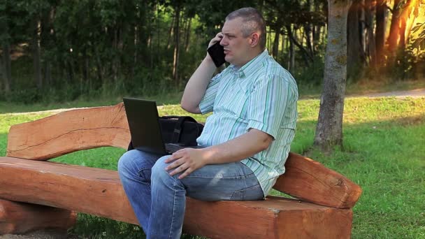Homem falando ao telefone no parque no banco — Vídeo de Stock