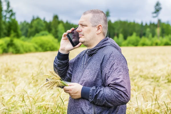 Farmer talking on cell phone near cereal field — Stock Photo, Image