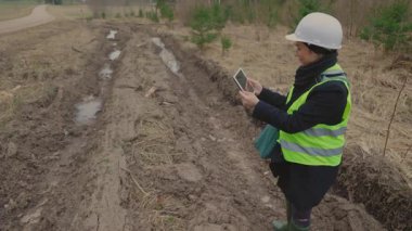 Çevre müfettişi, bir tablet bilgisayar kullanarak ormanda araba izlerinin fotoğraflarını çekiyor.