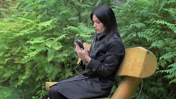Kobiet słuchać muzyki na ławce w parku — Wideo stockowe