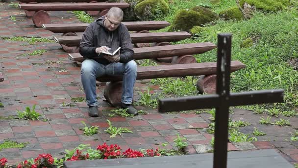 Homem no banco com a Bíblia na igreja ao ar livre — Vídeo de Stock