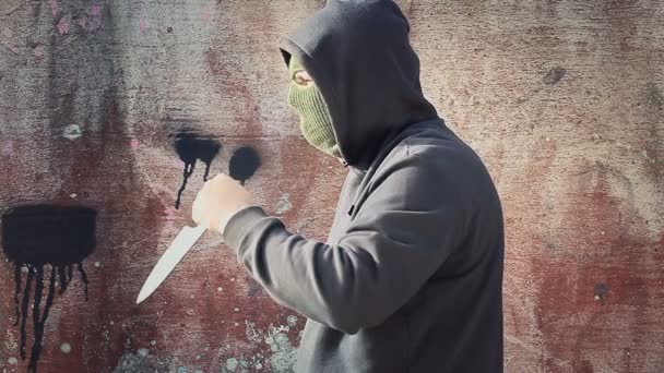 Hombre con cuchillo vestido con máscara cerca de la pared — Vídeos de Stock