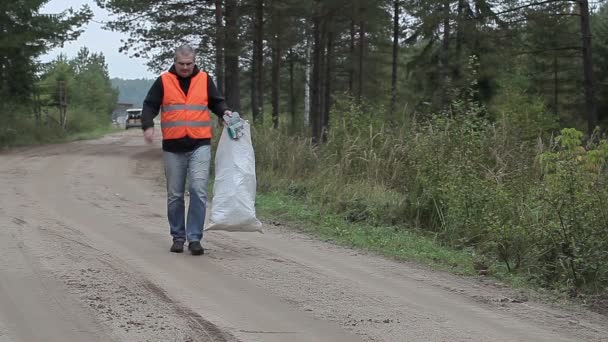 Man with cell phone and bag of plastic bottles on the road in forest — Stock Video