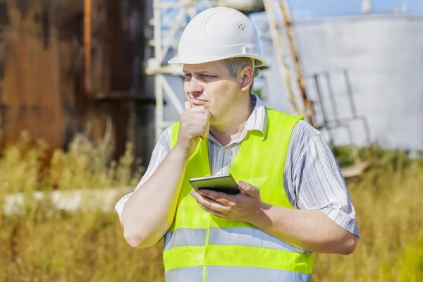 Thoughtful engineer using tablet PC near tanks — Stock Photo, Image