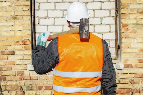 Bouwvakker met een moker op bakstenen muur — Stockfoto