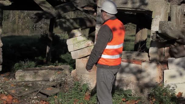 Stavební inspektor s smartphone v blízkosti opuštěných poškozené budovy — Stock video