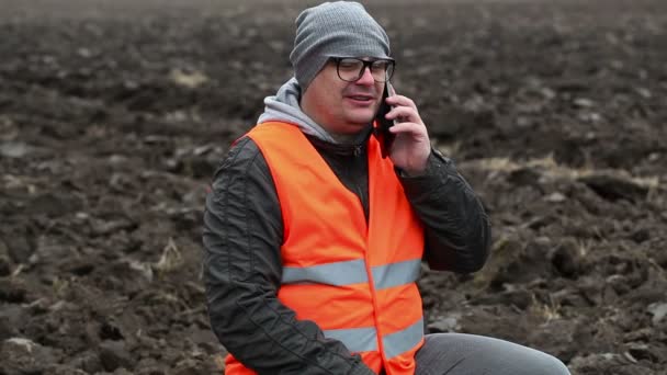 Bauer spricht auf dem gepflügten Feld mit Smartphone — Stockvideo