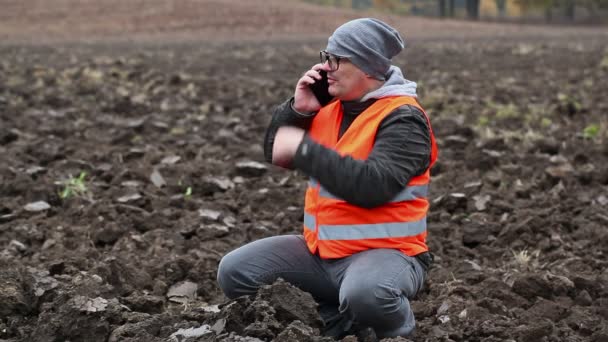 智能手机在犁过的田野上显示手势的农夫 — 图库视频影像