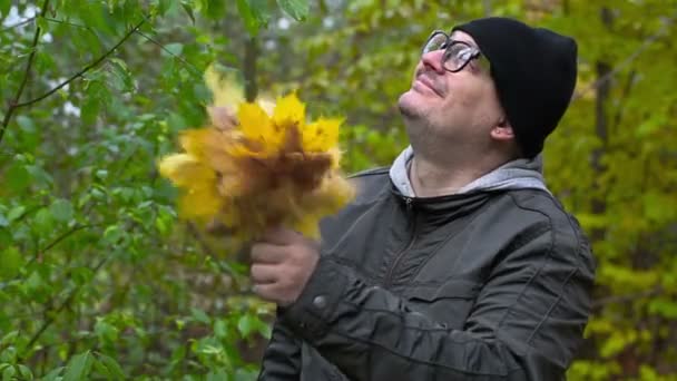 El hombre arroja hojas de otoño en el parque — Vídeo de stock
