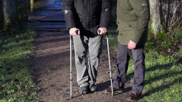 Hombre discapacitado en muletas con asistente al aire libre — Vídeos de Stock