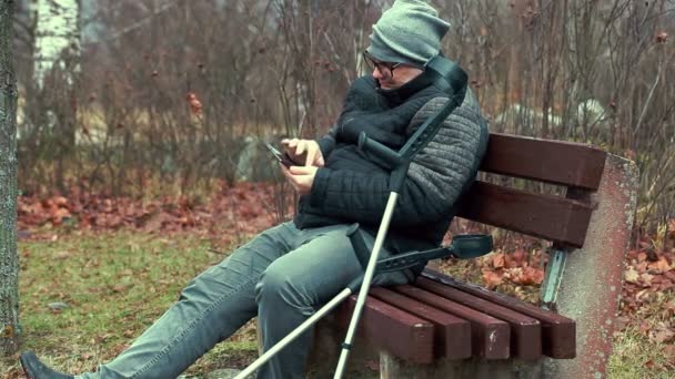 Disabled man with crutches and tablet PC on bench — Stock Video