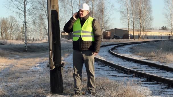 Arbetaren pratar på smartphone på hög spänning pol nära railway på vintern — Stockvideo