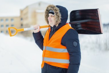 Worker with snow shovel near building in winter clipart