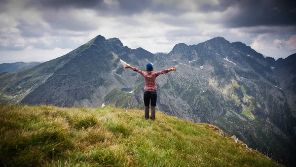 Mulher caminhante relaxante em um topo de uma montanha admirando picos rochosos circundantes — Fotografia de Stock