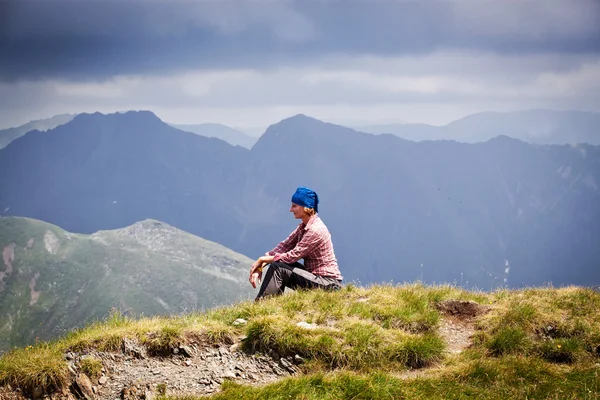 Wanderin entspannt sich auf einem Gipfel eines Berges und bewundert die umliegenden Felsgipfel — Stockfoto