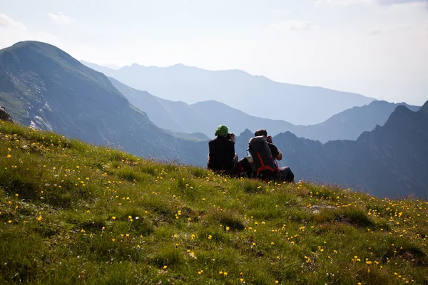 Casal de caminhantes admirando a vista e tirando fotos de altas montanhas — Fotografia de Stock