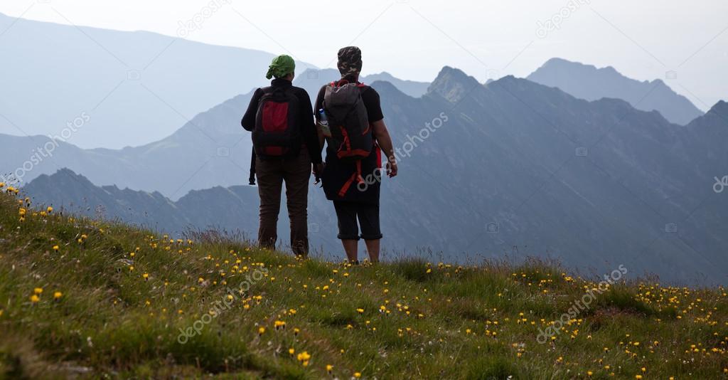 Couple of hikers admiring view and taking photographs of high mountains