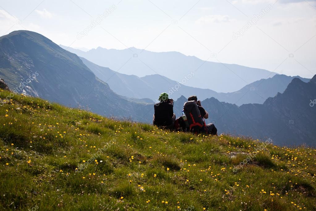Couple of hikers admiring view and taking photographs of high mountains
