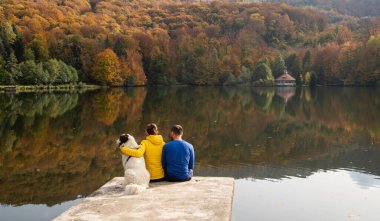 Güzel sonbahar gölü kenarında oturan çift ve köpek.