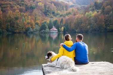 Güzel sonbahar gölü kenarında oturan çift ve köpek.