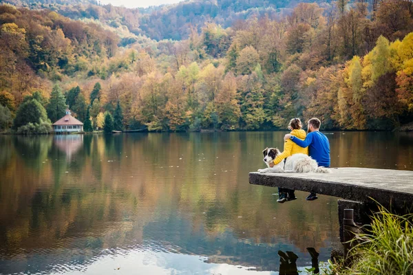夫婦と犬が美しい秋の湖のそばに座り — ストック写真