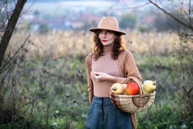 Sonbahar bahçesinde içi balkabağı dolu sepeti olan bir kadın.